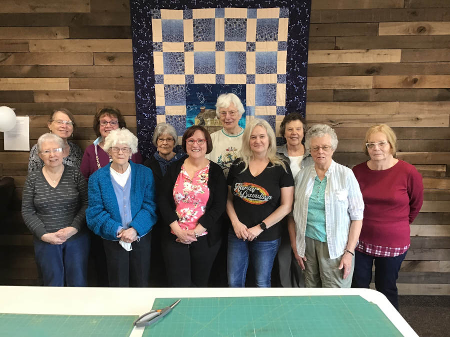 salvation stitchers group of ladies standing in front of quilt